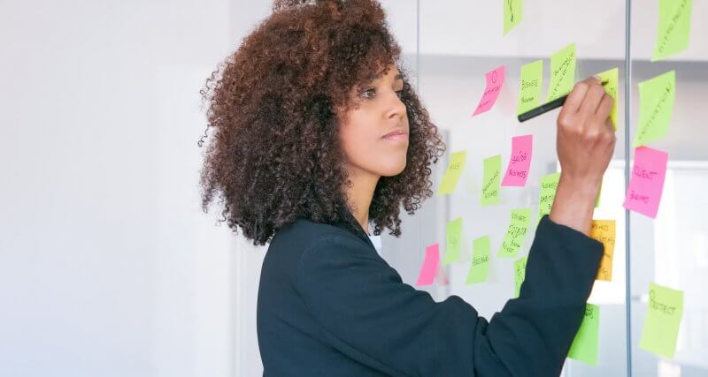 Mulher fazendo brainstorm para o planejamento de marketing de conteúdo com post its colados na parede