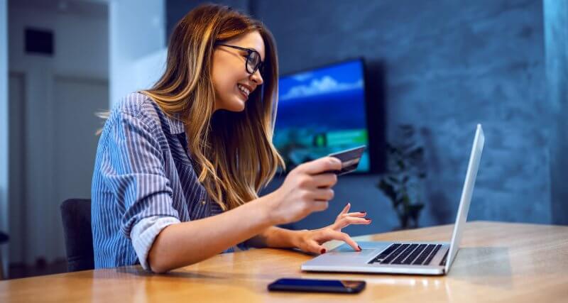 Mulher em frente ao notebook com o cartão de crédito na mão, fazendo compras na Black Friday 2021