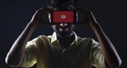 Homem segurando celular com o logo do YouTube em frente ao rosto