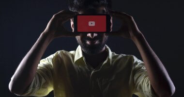 Homem segurando celular com o logo do YouTube em frente ao rosto