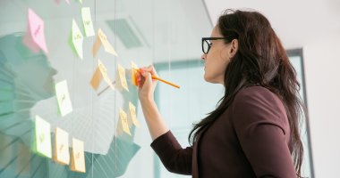 Profissional de marketing digital documentando ideias para o funil de conteúdo em post its na parede