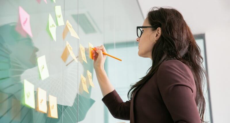 Profissional de marketing digital documentando ideias para o funil de conteúdo em post its na parede