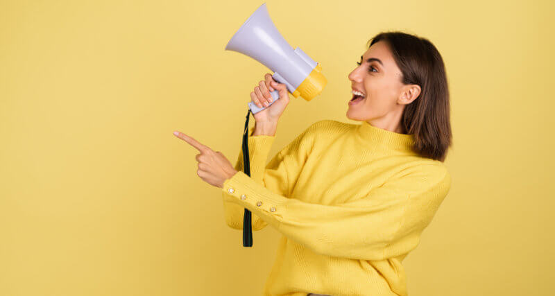 Mulher falando em um megafone em frente a um fundo amarelo