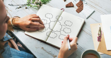 Mulher debruçada sobre uma mesa desenhando um mapa mental em um caderno