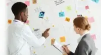 Duas pessoas criando um planejamento de comunicação em um quadro branco.
