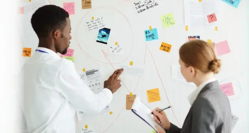 Duas pessoas criando um planejamento de comunicação em um quadro branco.